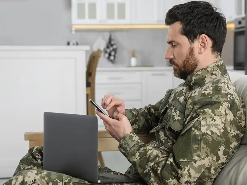 Military personnel in uniform using their phone and laptop
